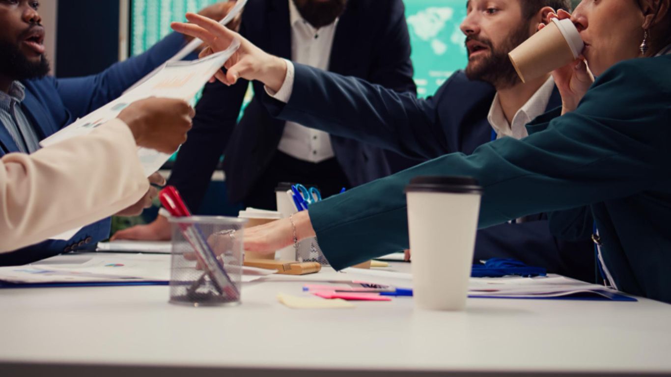 A professional non-native English speaker sitting in a modern office meeting, looking slightly frustrated while colleagues talk in the background, symbolizing being fluent in English but still misunderstood because of their accent.